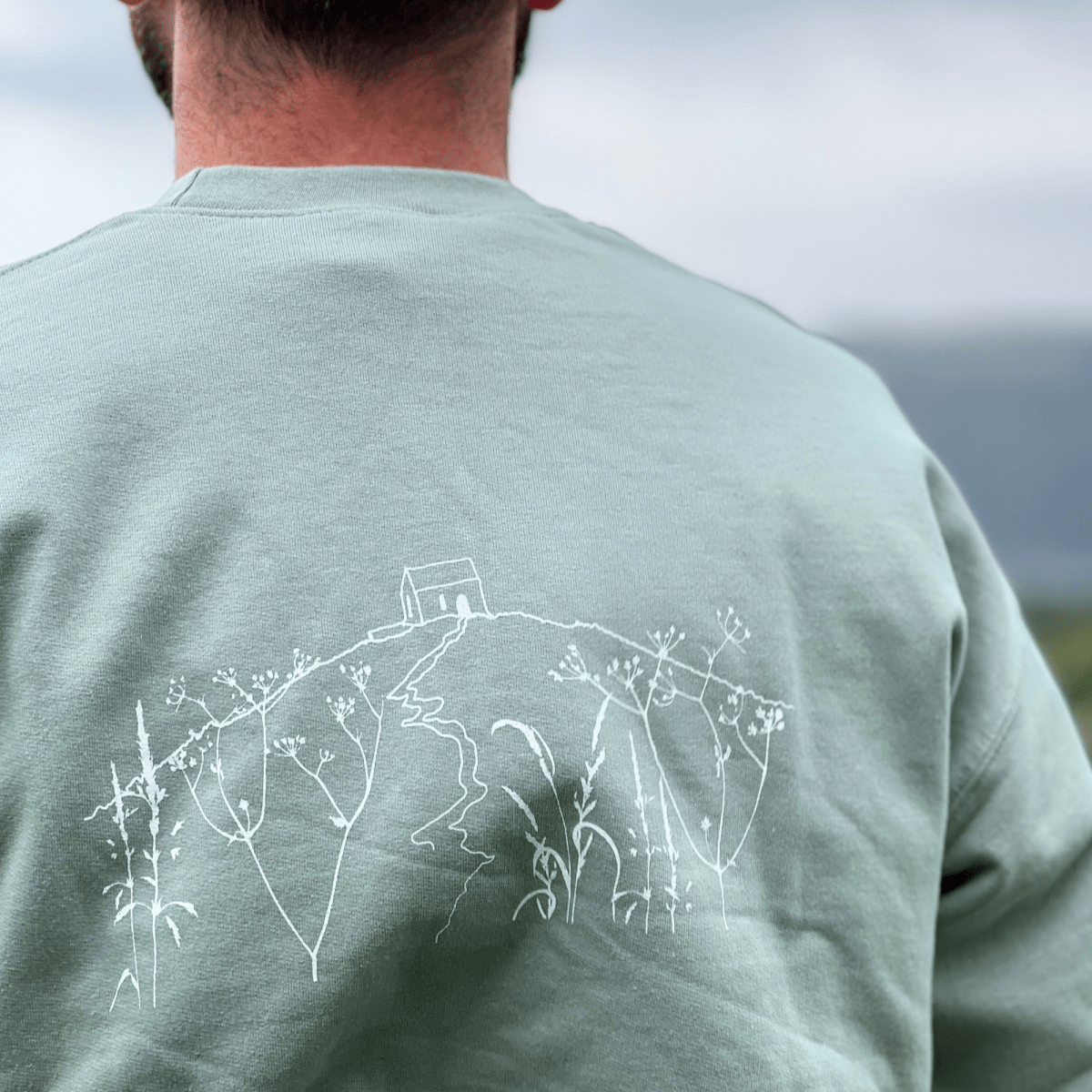 A  Sage Green  crewneck sweatshirt with 'RAME HEAD' printed in white on the chest With an illustration of Rame Head on the back from Helen Round