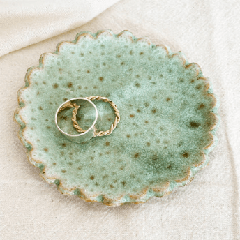 Two gold rings on a textured green ceramic dish with a white background, sold by Helen round