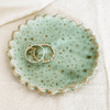 Two gold rings on a textured green ceramic dish with a white background, sold by Helen round