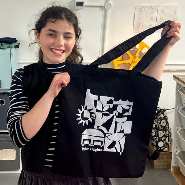 Person holding a black tote bag with white design and text in an indoor setting