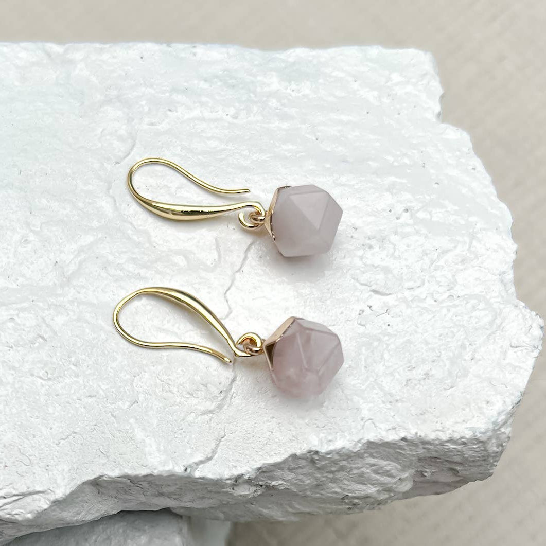 Pair of gold earrings with pink gemstones on a textured white surface sold by Helen Round