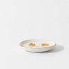 White jewelry dish with gold earrings on a light gray background