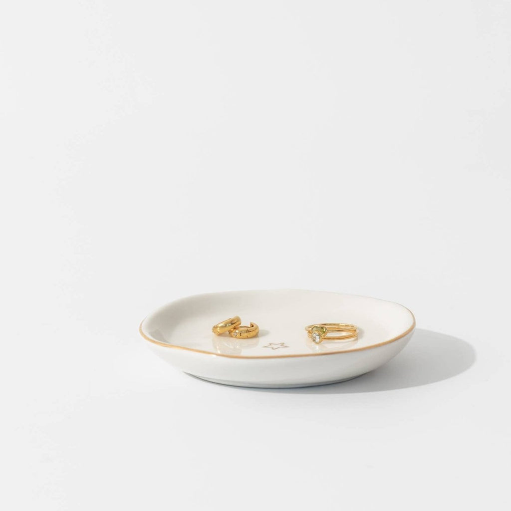 White jewelry dish with gold earrings on a light gray background