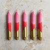 Five pink and gold gradient candles on a textured beige surface