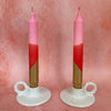 Two pink and gold candles in white holders on a pink background