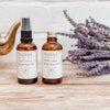 Two bottles of moksa daily calm cleansing oil on a wooden surface with lavender flowers.