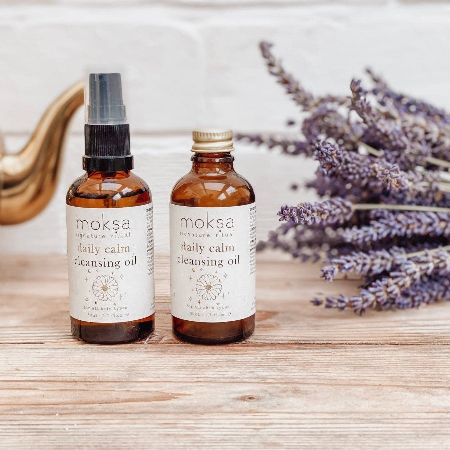 Two bottles of moksa daily calm cleansing oil on a wooden surface with lavender flowers.