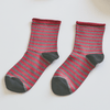 Red and gray striped socks on a light surface with a book and small box in the background Sold by Helen Round