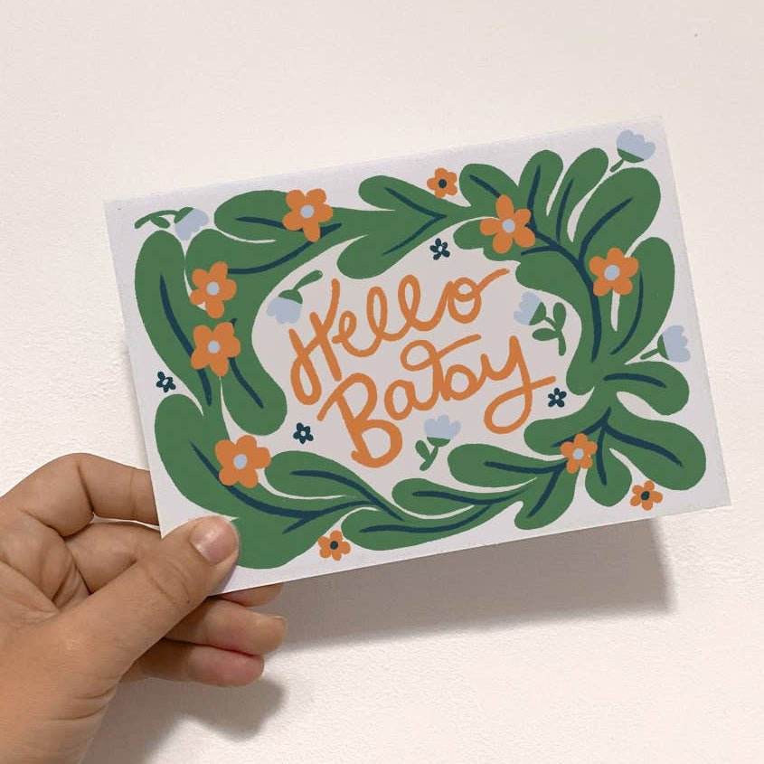 Hand holding a card with decorative text and green wreath design on a light background  sold by Helen Round