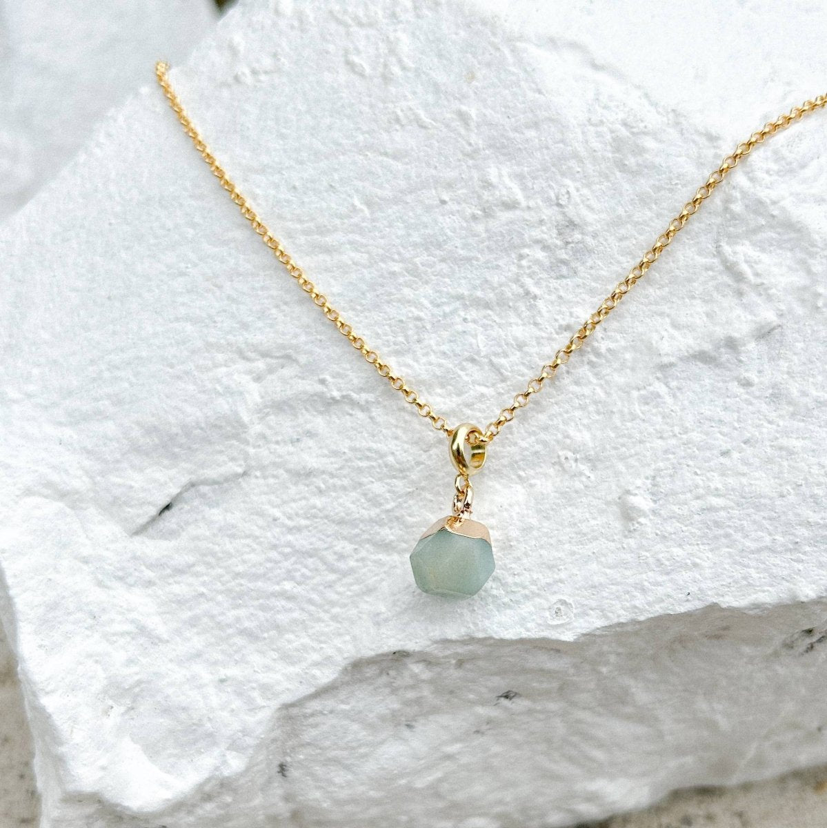 Gold necklace with a green pendant on a white stone surface sold by Helen Round