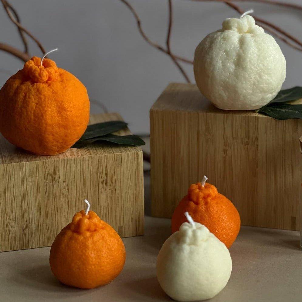Decorative candles shaped like oranges on wooden blocks with a neutral background