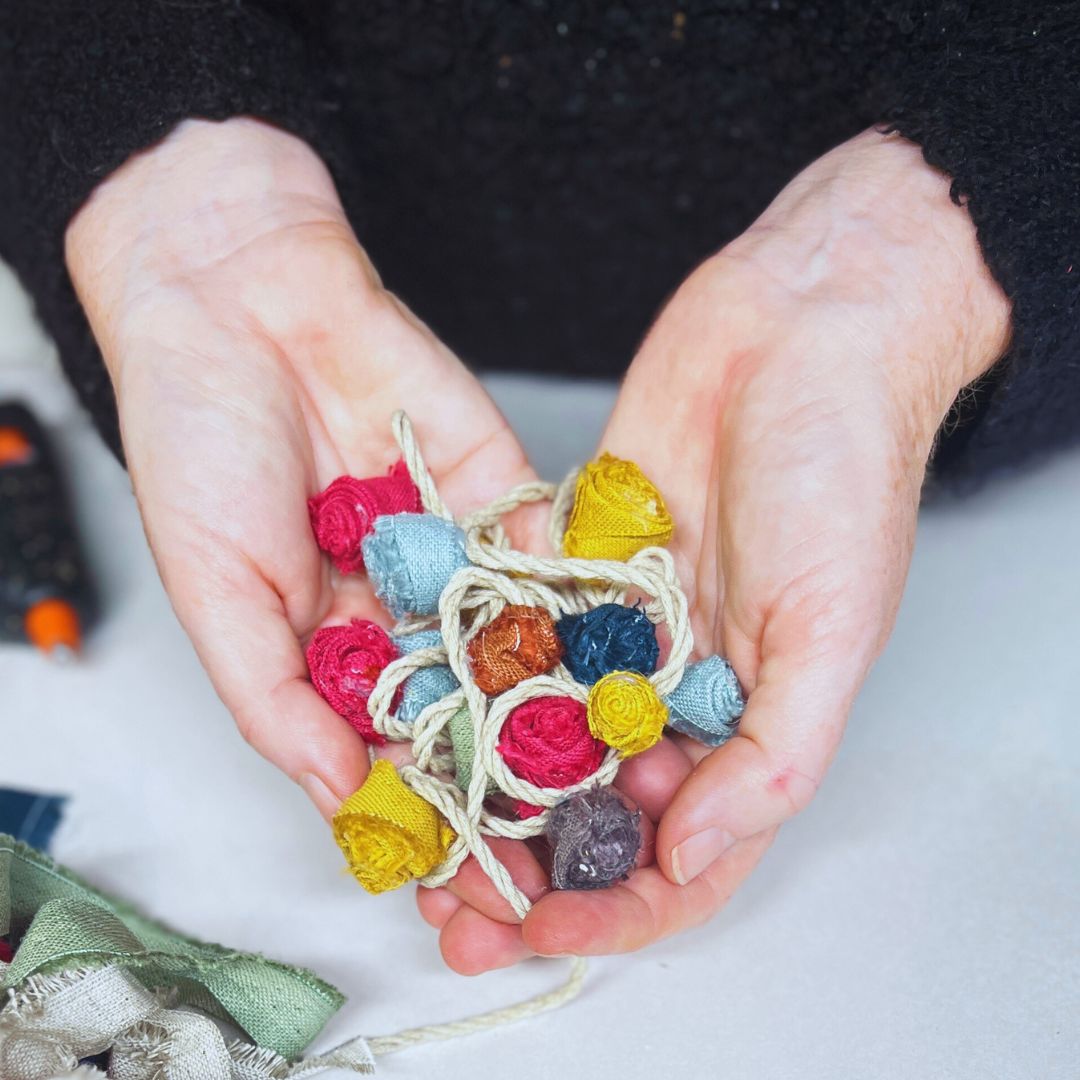 DIY Linen Rose Garland cupped in hands with multi coloured hand made roses on linen twine